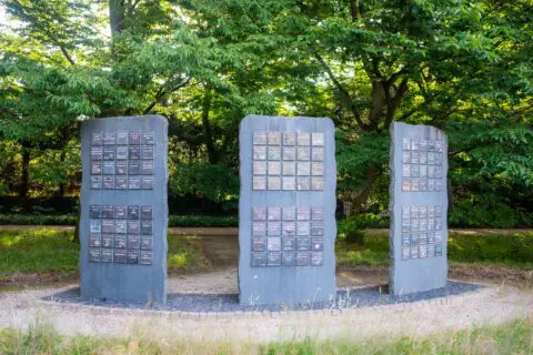 Drie rechtopstaande gedenkpanelen tussen de bomen in de gedenktuin.
