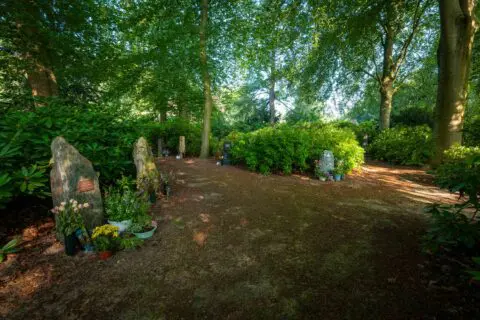 Gedenkbeeld tussen bomen en bloeiende beplanting in de tuin van Crematorium Kranenburg.