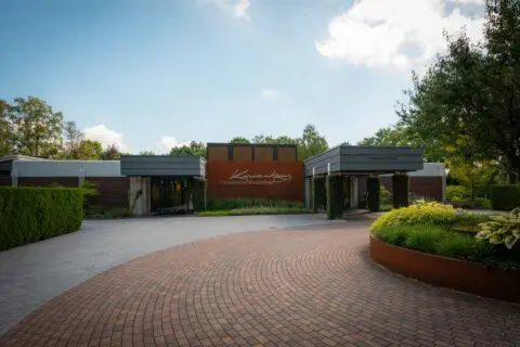 Crematorium Kranenburg gezien vanaf het voorplein met bomen en beplanting.