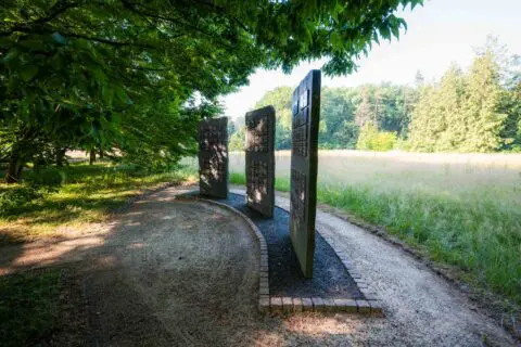 Wandelpad langs drie gedenkpanelen aan de rand van een open veld.