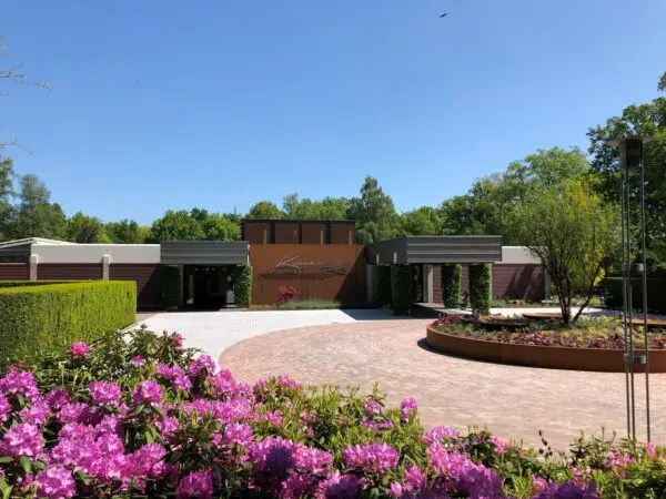 Voorzijde van Crematorium Kranenburg met de entree, het voorplein en bloeiende bloemen.